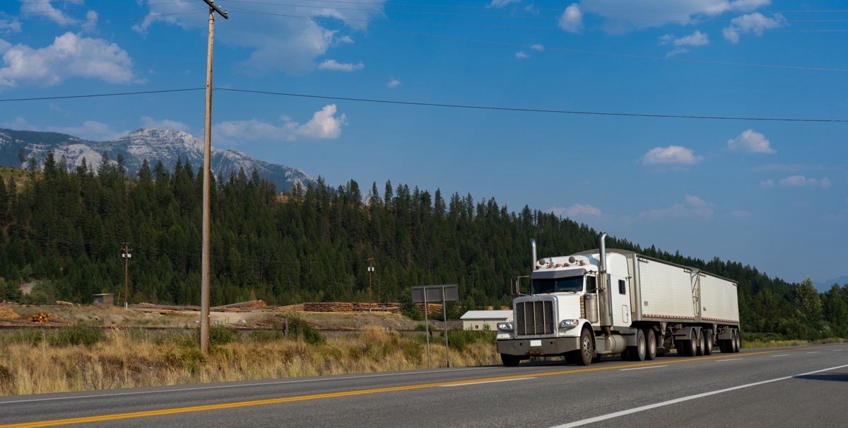White semi truck on a mountain highway near a lumber yard