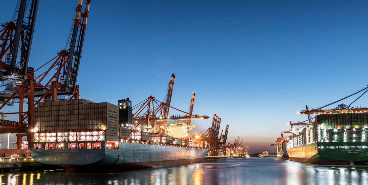 Container ships docked under cranes at a port at twilight