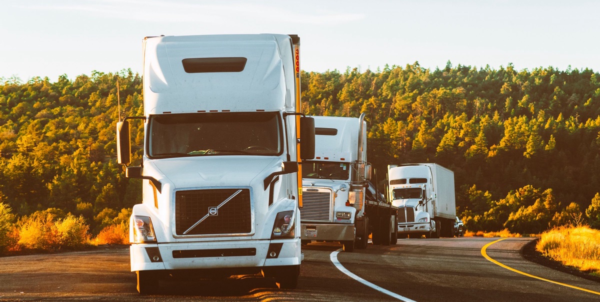 Three white semi trucks driving on a highway at sunset