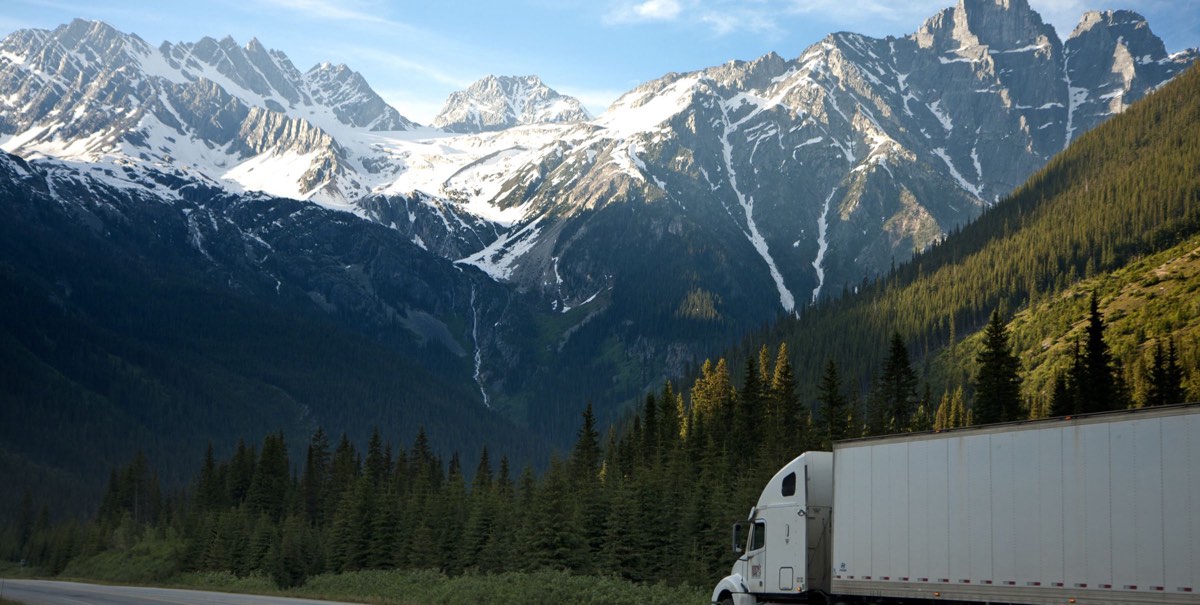 White semi-truck on a highway below snow-capped mountains in the Canadian Rockies